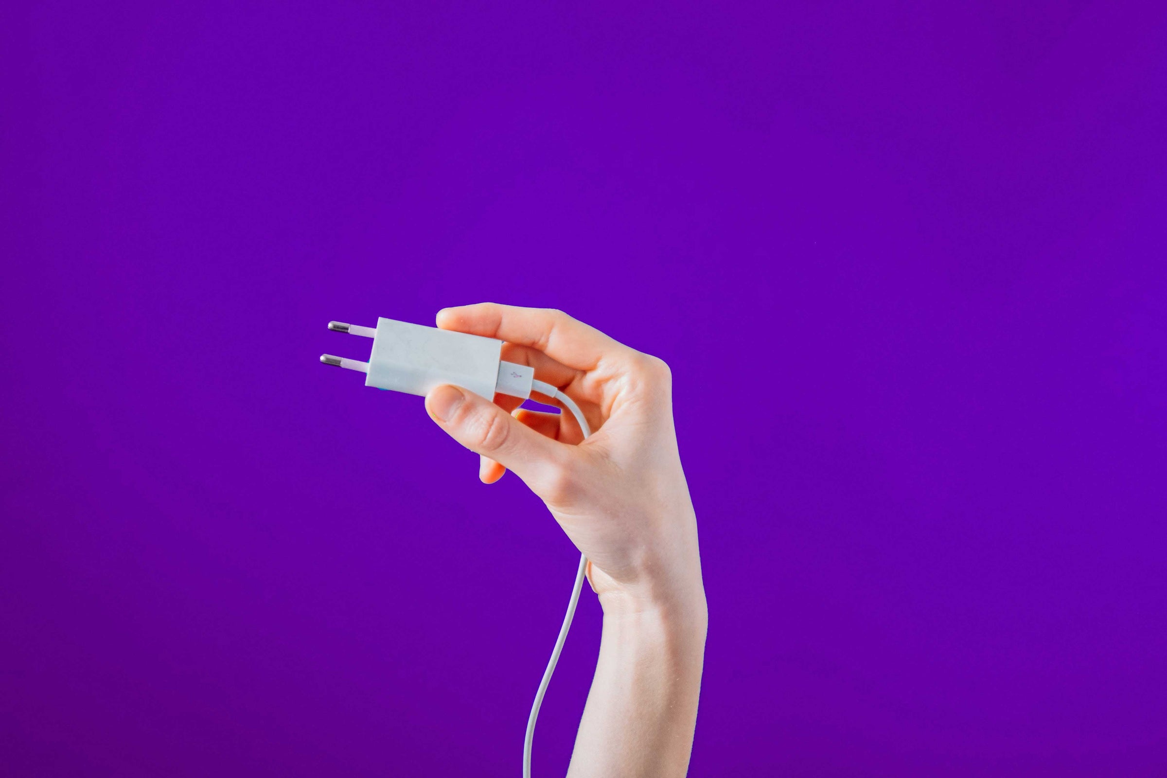Woman holding Europe travel adapter against purple wall