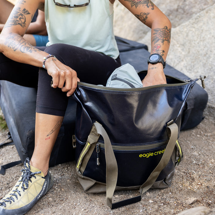 Woman on hike looks through her black Eagle Creek Migrate Tote Bag