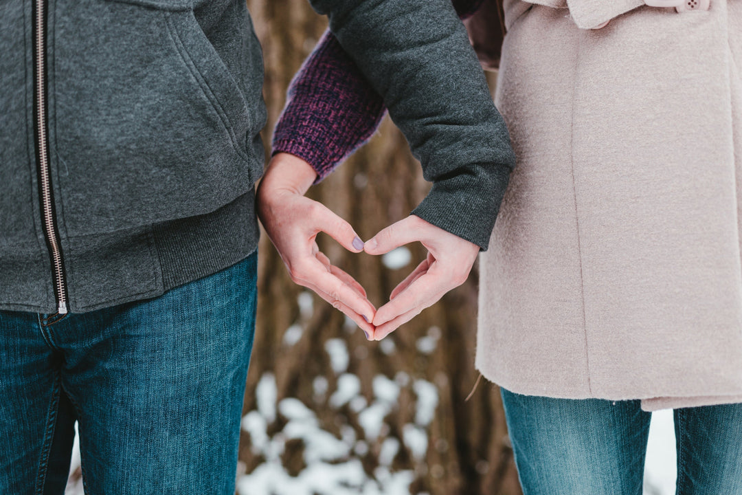 Couple make heart symbol with hands while standing in snowy Banff Canada