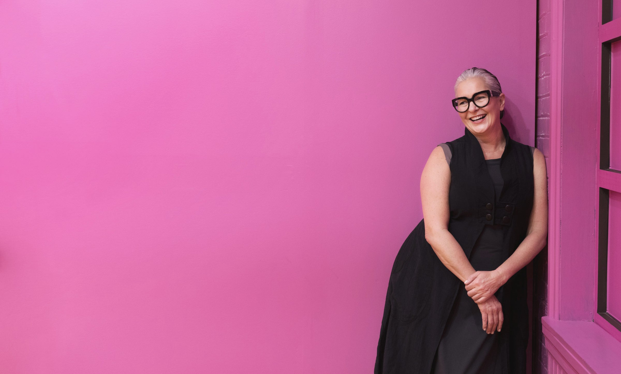 woman standing against pink wall wearing travel clothing