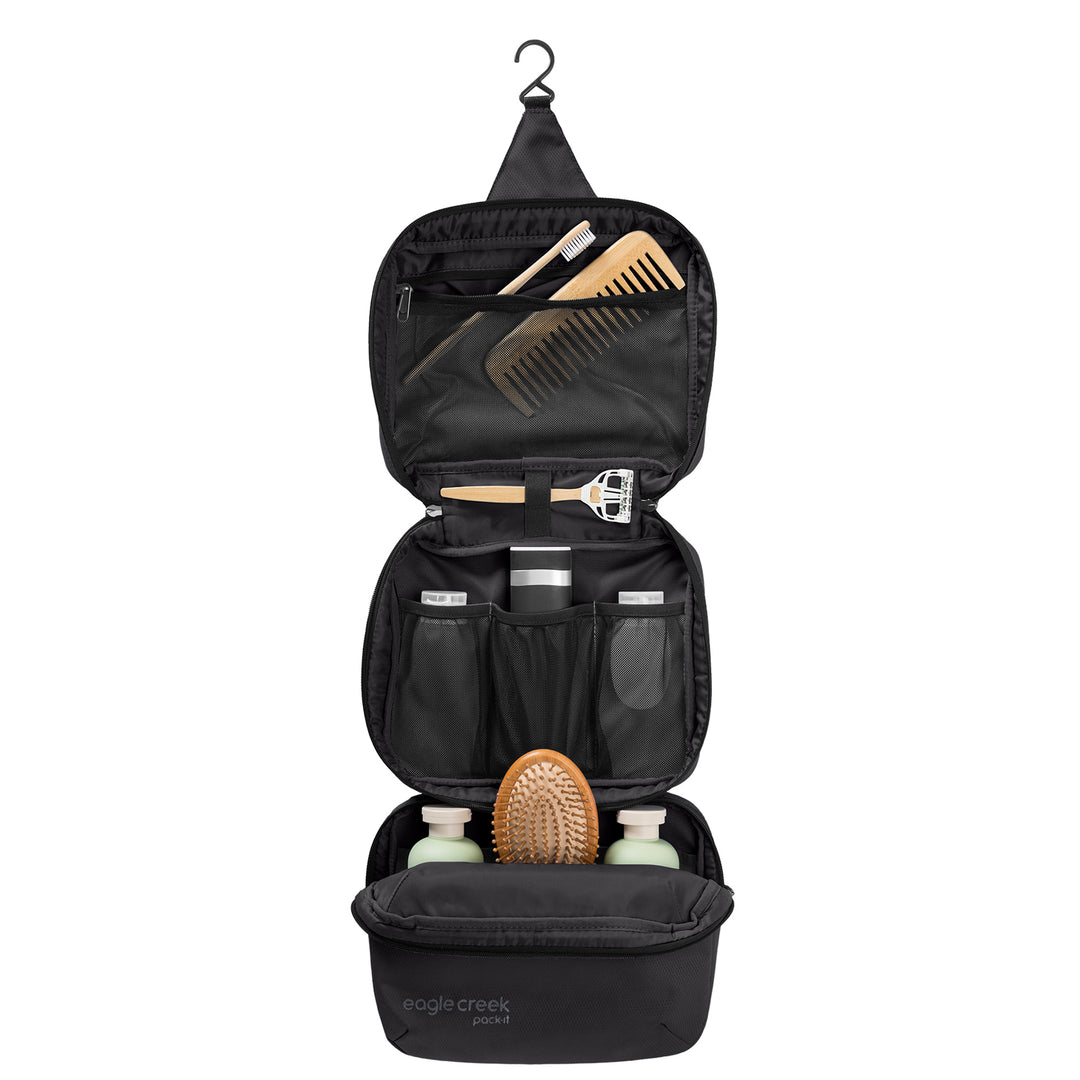 Black Eagle Creek Pack-It® Trifold Toiletry Kit hanging open with black lining packed with hair brush body wash razor comb
