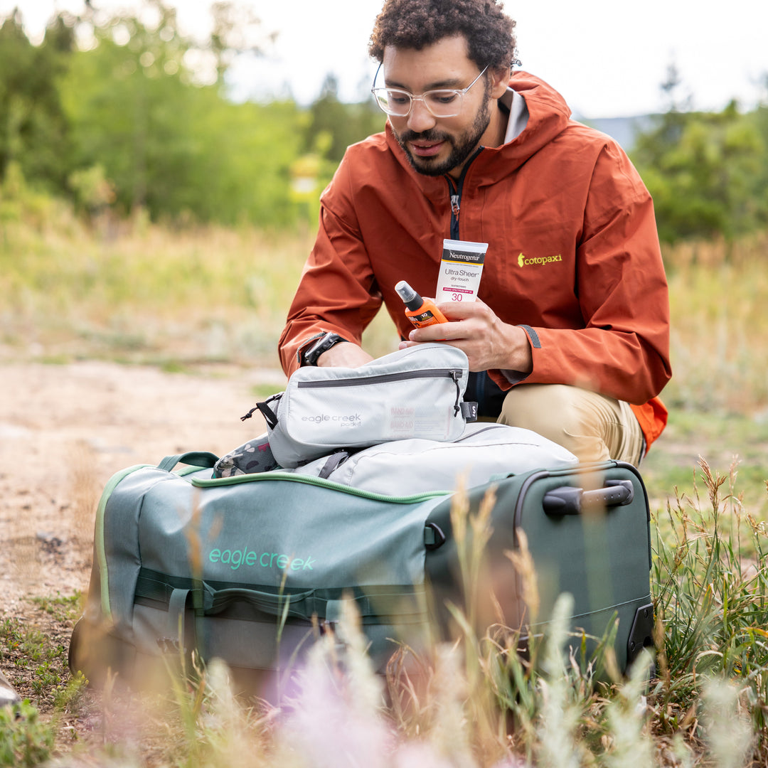 Man packing his green Eagle Creek Migrate 40L Duffel Bag while camping