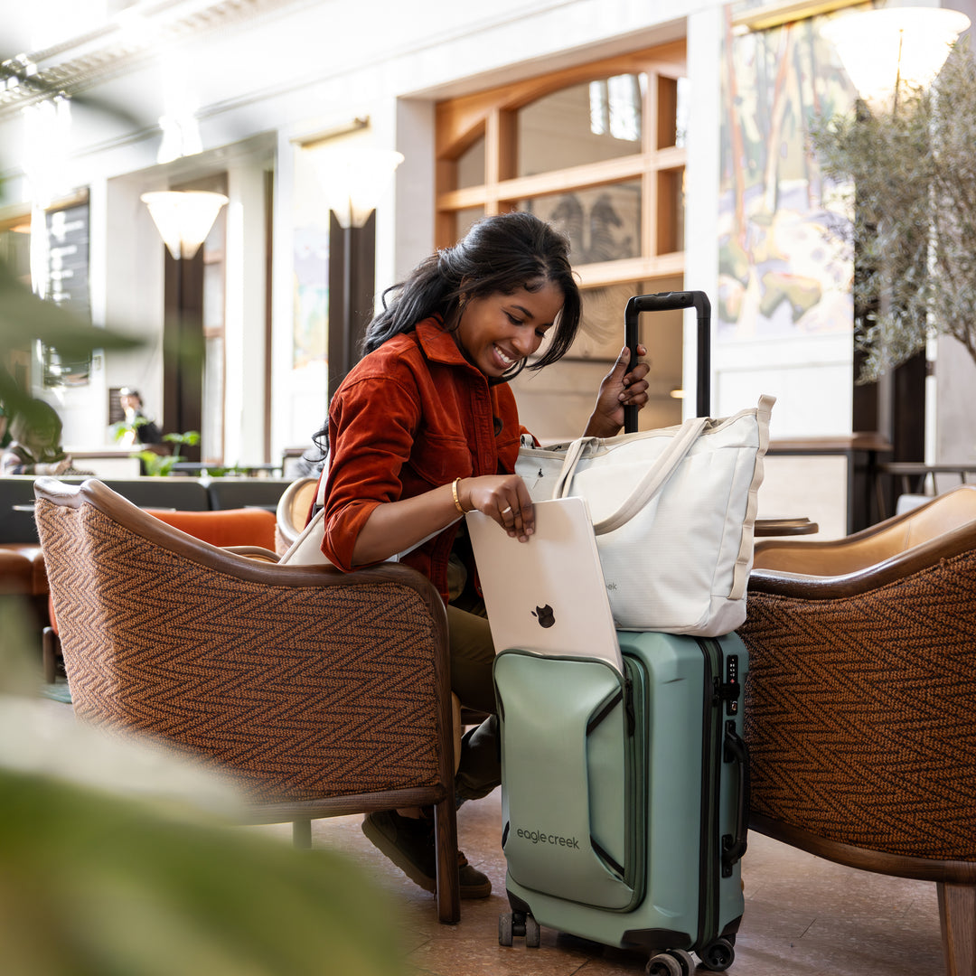 Woman putting laptop away in airport lounge Eagle Creek Tarmac 4 Wheel Carry On Luggage
