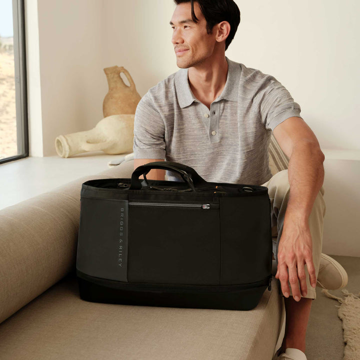 Man Sits in hotel room by window with ZDX overnighter bag in black