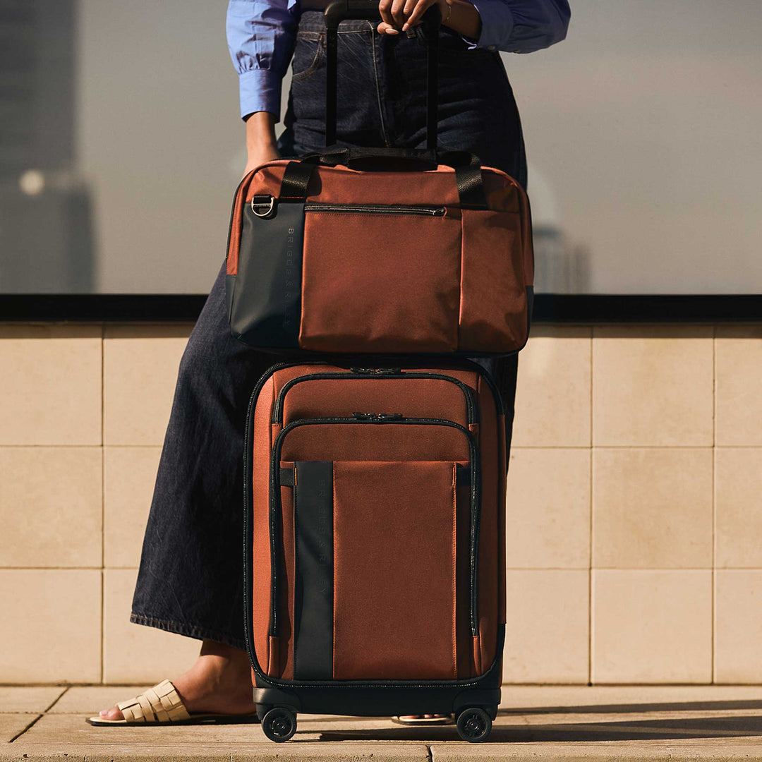 Woman with Briggs Riley Carry On spinner and tote in color Canyon Orange