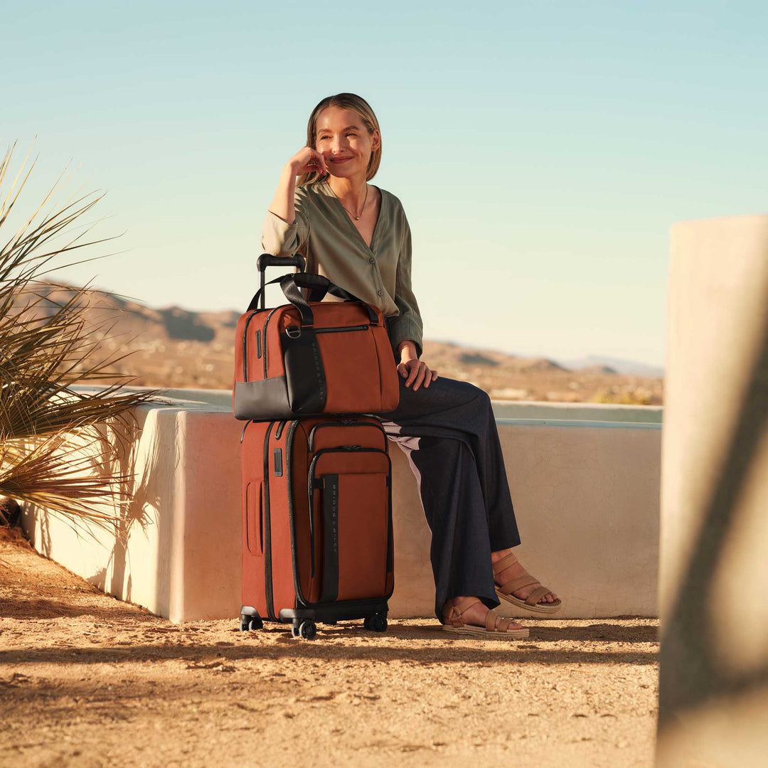 Woman sitting at resort with orange Cabin Bag and matching wheeled carry on
