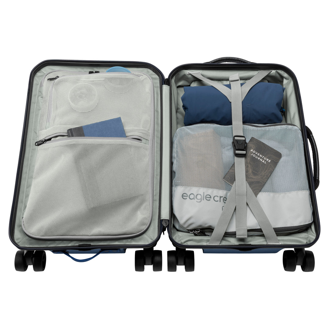 Interior of blue suitcase with grey lining packed wit clothes and book Eagle Creek Tarmac 4 Wheel Carry On Luggage