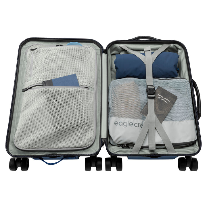 Interior of blue suitcase with grey lining packed wit clothes and book Eagle Creek Tarmac 4 Wheel Carry On Luggage