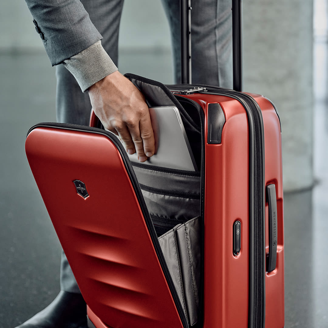 Man slides laptop into front pocket of hardside swiss army carry on suitcase
